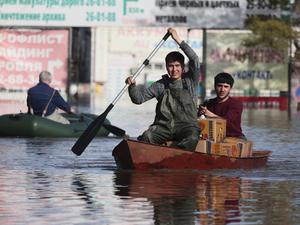Zwei Männer rudern ein Boot durch das Hochwasser eines überschwemmten Gebiets.