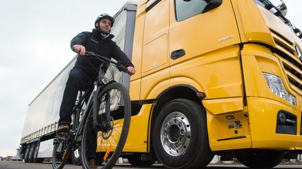 Ein Radfahrer steht mit seinem Fahrrad in der Versuchsabteilung von Mercedes Benz neben einem LKW mit einem Abbiegeassistenten. 