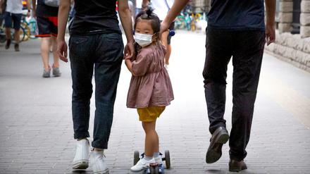 Ein kleines Mädchen mit Mundschutz wird auf ihrem Roller über einen Gehweg in Peking gezogen.