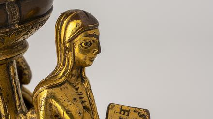 Die Personifikation von Afrika hält ein Buch mit der Aufschrift „SCIENTIA“ (Wissenschaft). Sie sitzt auf einem Bronzeleuchter, der um 1180 entstand. 