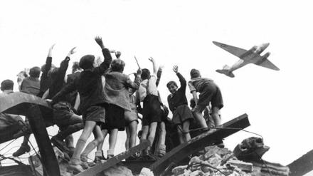 Luftbrücke live: Von einem Trümmerberg winken West-Berliner Kinder einem Propellerflugzeug zu.