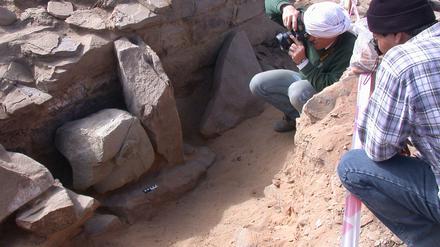 Kopfunter „bestattet“: Erste fotografische Dokumentation des Statuenkopfes 2004 in der Oase Tayma in Saudi Arabien. Der Entdecker, DAI-Archäologe Arnulf Hausleiter, ist rechts im Bild, mit Kamera und weißem Turban.