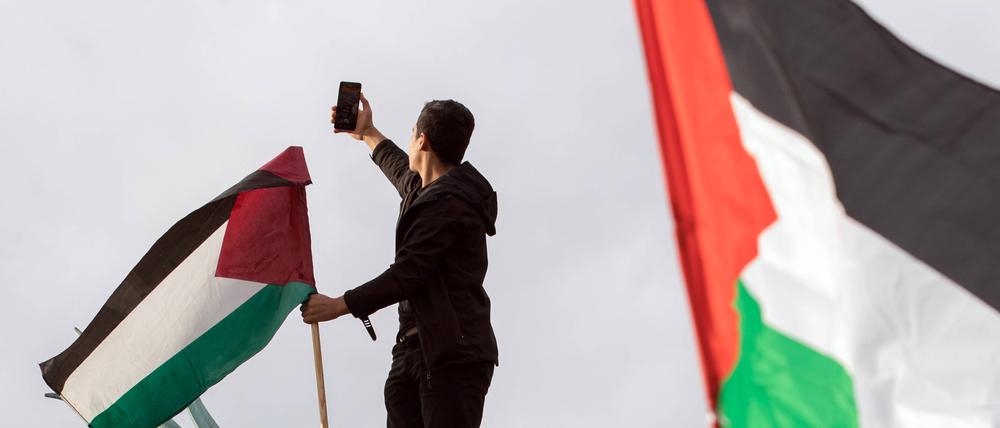 Eine Pro-palästinensische Großdemonstration im November 2023 in Berlin. Ein Mann ist auf den Neptunbrunnen geklettert und fotografiert sich mit einem Smartphone. 