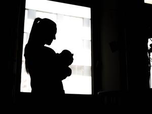 Eine Frau steht mit einem Neugeborenen am Fenster einer Klinik.