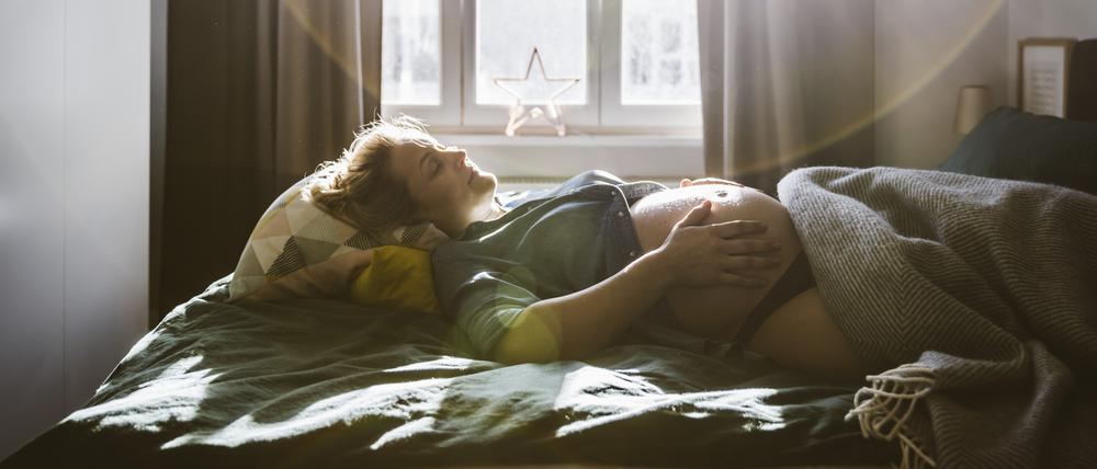 Eine schwangere Frau liegt im Bett und hält ihren nackten Bauch (Symbolbild).
