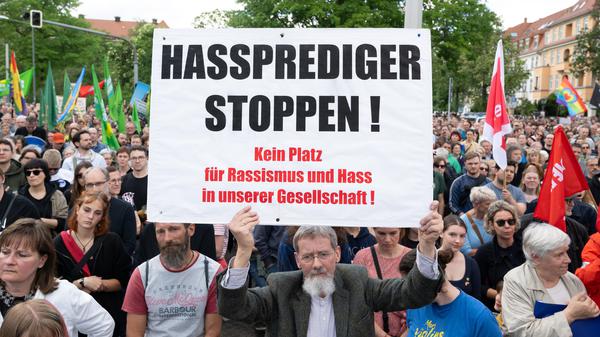 Teilnehmer einer Kundgebung stehen auf dem Pohlandplatz und halten ein Schild mit der Aufschrift ·Hassprediger stoppen·. 
