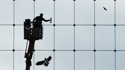 Ein Gebäudereiniger ist als Silhouette zu sehen, während er eine gläserne Fassade putzt. 