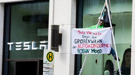 Ein Aktivist hängt bei einer Protestaktion der Umwelt- und Naturschutzorganisation Robin Wood gegen die geplante Tesla-Werkserweiterung in Grünheide vor dem Tesla Store in der Mall of Berlin in einem Tripod und hält ein Transparent. 