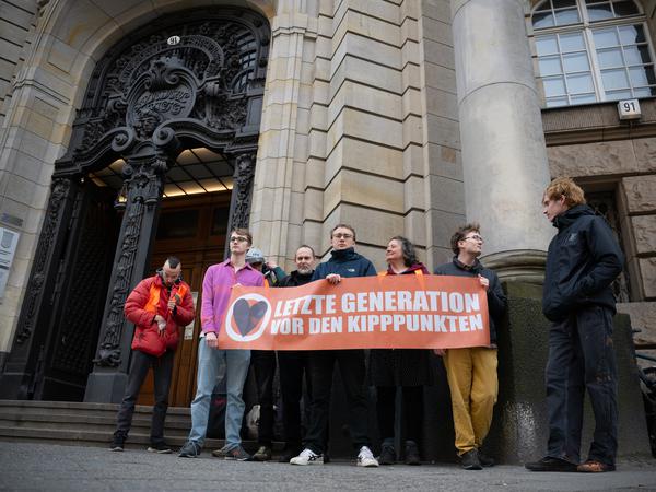Klimaaktivisten der Letzten Generation stehen vor dem Kriminalgericht Moabit mit einem Transparent.