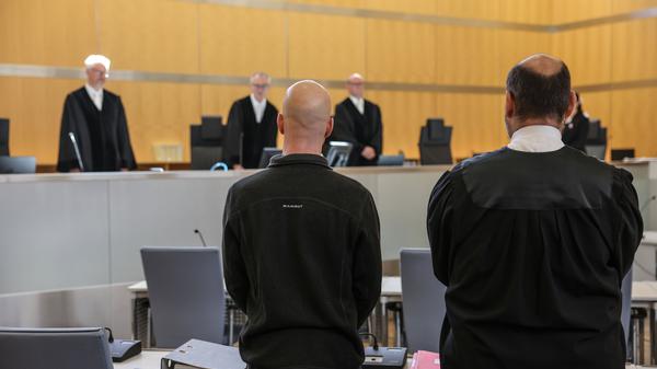 Der Angeklagte (l, vorne) steht neben seinem Anwalt Marvin Schroth (r) im Gerichtssaal. 