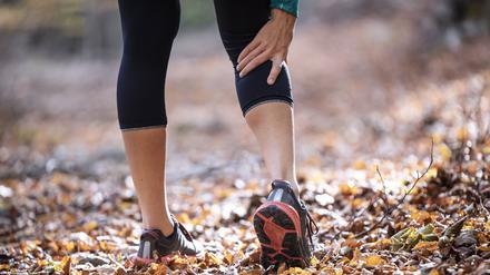 Sportswoman having cramp in leg while standing on forest path model released Symbolfoto JSRF01246