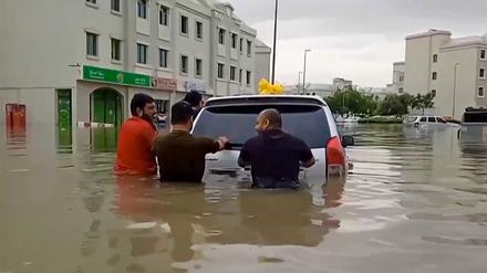 Menschen schieben auf einer überfluteten Straße in Dubai ein Auto.