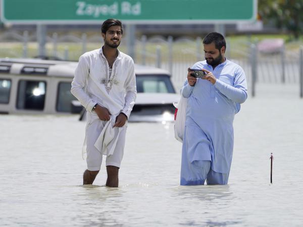 Zwei Männer waten durch eine überschwemmte Straße in Dubai. Ihre Autos mussten sie verlassen.