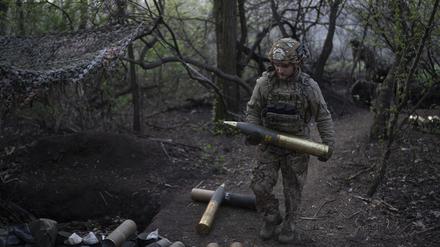 Ein ukrainischer Soldat trägt eine Granate für eine Haubitze an der Front.