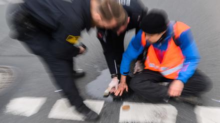 Polizisten versuchen festgeklebte Hände von Aktivisten der Gruppierung «Letzte Generation» am Deisterkreisel in Hannover mit Speiseöl von der Straße abzulösen. 