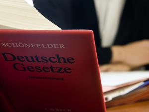 Ein Anwalt sitzt hinter der aufgeschlagenen „Schönfelder Textsammlung Deutsche Gesetze“ in einem Gericht (Symbolbild).