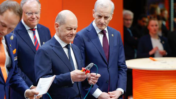 Bundeskanzler Olaf Scholz (SPD) schneidet ein Stück einer Datenleitung aus einem nachhaltigen, biobasierten Mantelmaterial zur industriellen Anwendung ab am Stand von Lapp auf der Hannover Messer. 