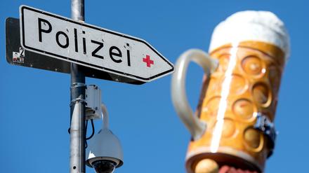 Eine Videokamera und ein Schild mit der Aufschrift "Polizei" hängen auf dem Münchner Oktoberfestgelände. Im Hintergrund ist ein Bierkrug auf einem Festzelt zu sehen.