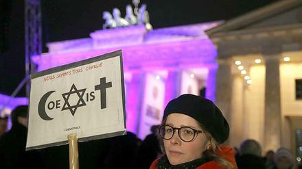 Eine Frau vor dem Brandenburger Tor mit einem Plakat, das die Gemeinschaft von Islam, Judentum und Christentum zeigen soll.