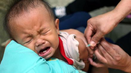 In einem Armenviertel von Manila wird ein Kind von Mitarbeitern des Roten Kreuzes gegen Masern geimpft.