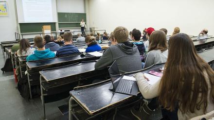 Studierende sitzen in einem Hörsaal, vorne hält eine Dozentin ihre Vorlesung.