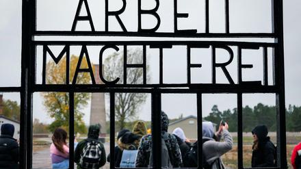 Hinter dem Lagertor mit dem "Schriftzug Arbeit macht frei" steht eine Gruppe von Jugendlichen auf dem Gelände des ehemaligen Konzentrationslagers.