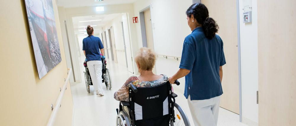 Zwei Pflegerinnen schieben Patienten mit Rollstühlen durch einen Flur. 