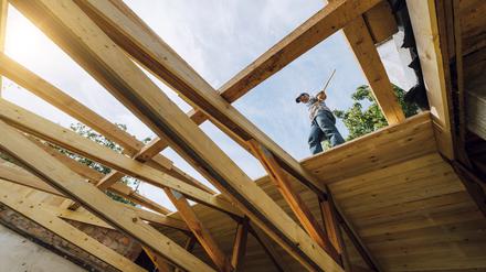 Ein Mann balanciert auf einem Holzbalken auf einer Baustelle. 