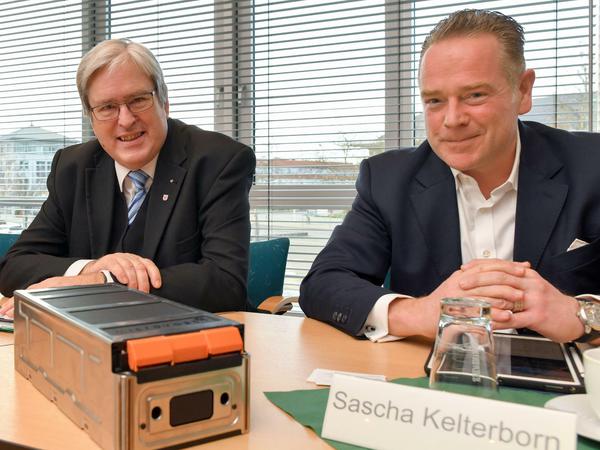 Brandenburgs Wirtschaftsminister Jörg Steinbach (l, SPD) und Sascha Kelterborn aus einer Pressekonferenz Ende 2019. Auf dem Tisch im Vordergrund liegt ein Batteriespeicher. 