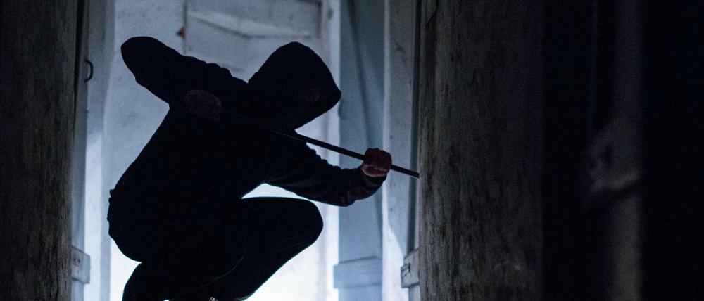 Ein fiktiver Einbrecher hebelt am mit einem Brecheisen eine Tür im Keller eines Wohnhauses auf.