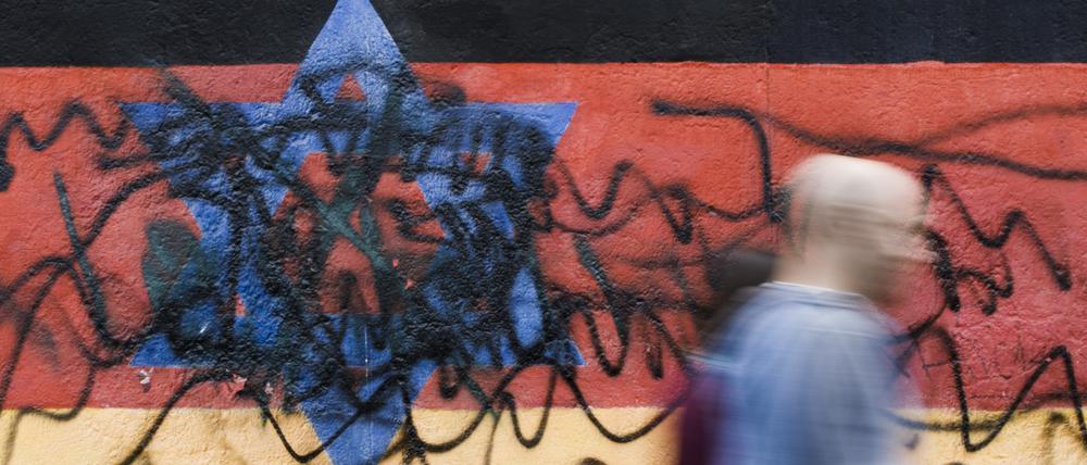 Passanten gehen an dem zerstörten Wandbild des Künstlers Günther Schäfer an der East Side Gallery vorbei. Das Wandbild „Vaterland“, das die schwarz-rot-goldene Deutschlandfahne mit einem blauem Davidstern zeigt, wurde von Unbekannten mit schwarzen Graffiti beschmiert.
