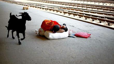 Eine Frau in Bangladesch schläft mit ihrem kleinen Sohn auf dem Bahnsteig. Eine Ziege läuft vorbei.