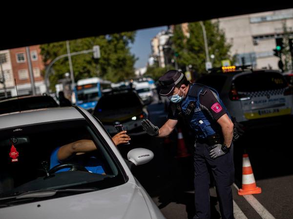 Ein Polizist spricht mit einem Fahrer an einem Kontrollpunkt in einem abgesperrten Stadtteil in Madrid. 