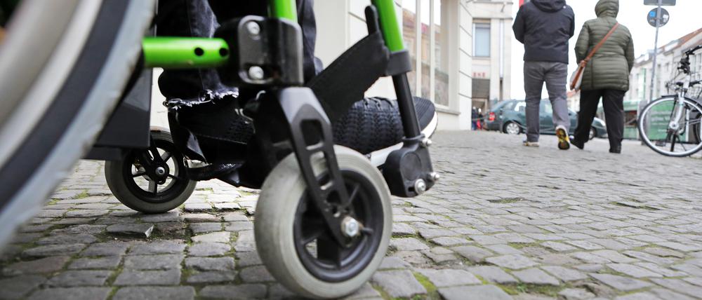 Behinderte, Rollstuhlfahrer im öffentlichen Stadtraum, Barrierefreiheit. Geschäfteingänge. Gehwegpflasterung.