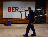 Installateur trägt Leiter vor einem BER-Schriftzug.