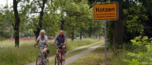 Ein älteres Paar auf Rädern passiert das Ortsschild der Gemeinde - Kotzen im Havelland.