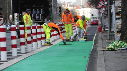 Arbeiter bringen einen Farbbelag für den geschützten Radweg auf. 