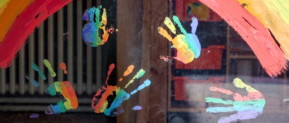 Kinderhände und ein Regenbogen sind an einer Kita zu sehen.