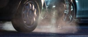 Ein Radfahrer steht neben einem Auto, dessen Abgase in der kalten Morgenluft sichtbar werden.