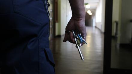 Eine Hand hält ein Schlüsselbund und im Hintergrund der Gang eines Gefängnisses verbrechen.