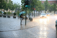Eine Passantin steht mit einem Schirm bei Starkregen am Luisenplatz. 