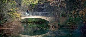 Eine Radfahrerin fährt im Sonnenschein über eine Brücke im Tiergarten.