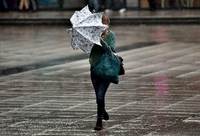 Eine junge Frauen kämpft in Berlin bei Starkwind mit einem Regenschirm.