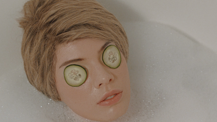 Eine Puppe liegt in einer Badewanne und hat Gurken auf den Augen.