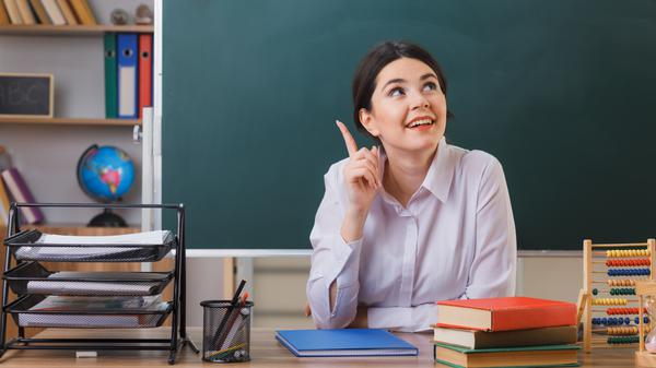 Eine junge Lehrerin sitzt in einem Klassenzimmer. (Symbolbild)