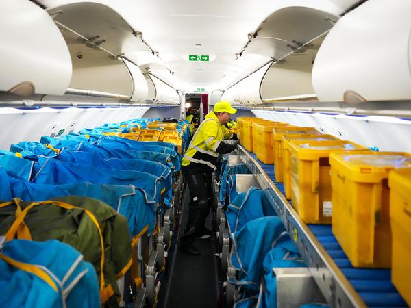 Gelbe Plastikboxen der Deutschen Post in der Kabine eines Airbus A320-214.