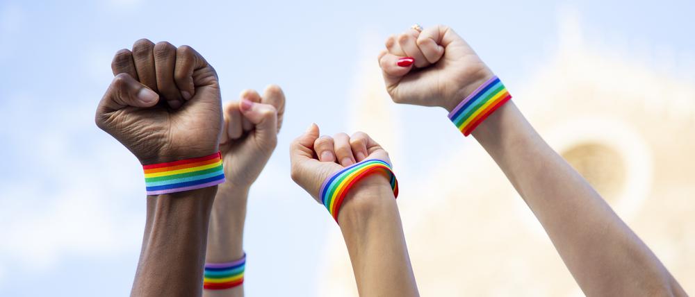 Hände mit queeren Armbändern fordern LGBTIQ-Rechte ein.
