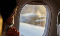Eine Fluggästin mit Maske schaut vor dem Start aus dem Fenster.