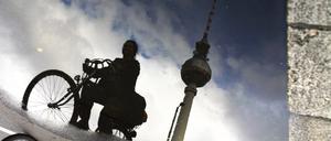 Radfahrerin spiegelt sich in Pfütze mit Fernsehturm am Alexanderplatz in Berlin.