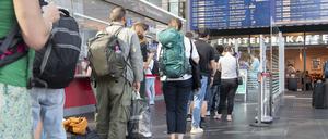  Reisende stehen im Berliner Hauptbahnhof am DB-Infoschalter.
